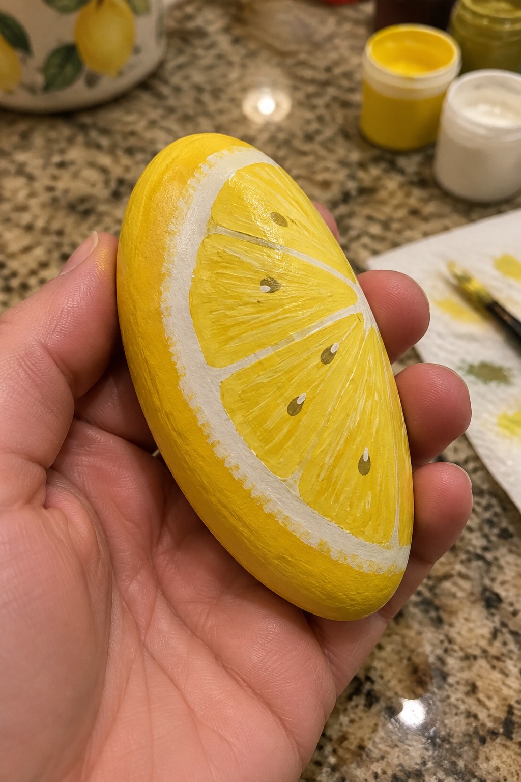 Hand holding yellow painted rock resembling lemon slice with white segments