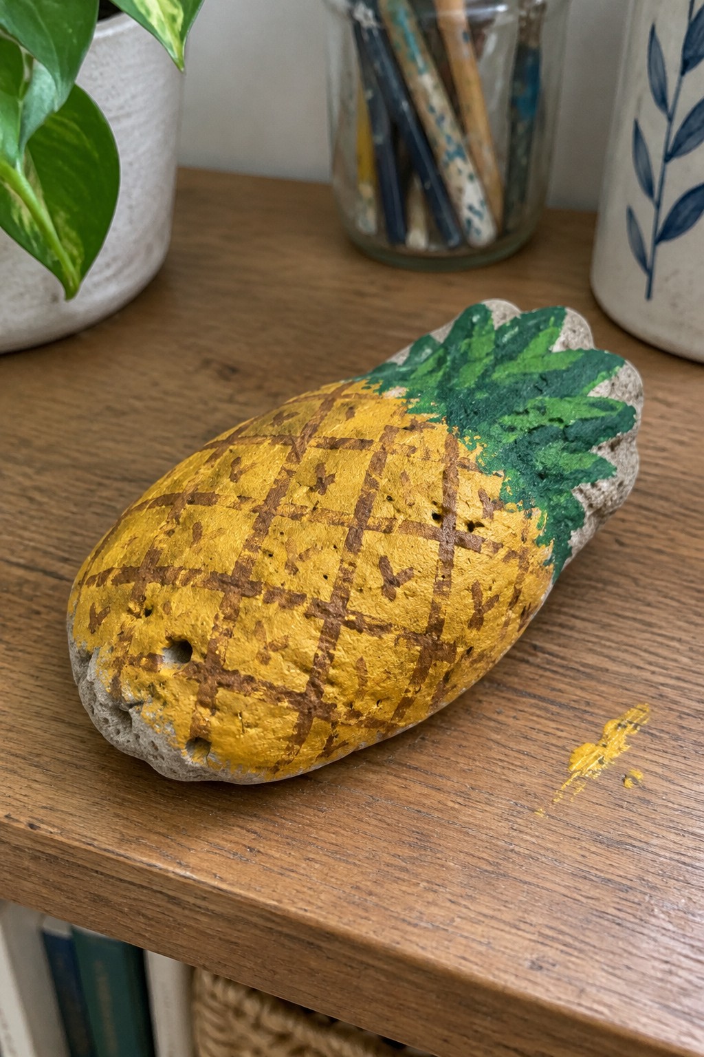 Yellow painted pineapple rock with green leaves on wooden table