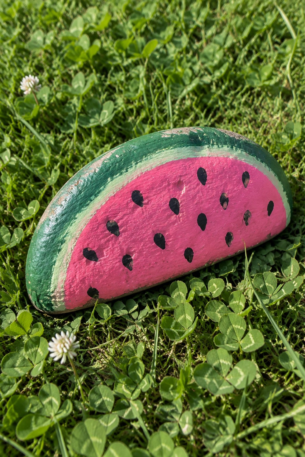 Painted rock resembling watermelon slice with black seeds on green grass
