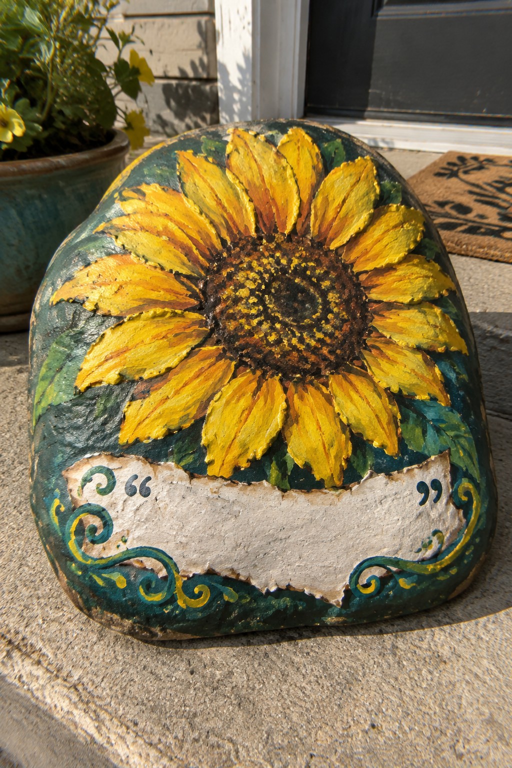 Painted rock with large yellow sunflower, green leaves, and blank decorative banner on steps