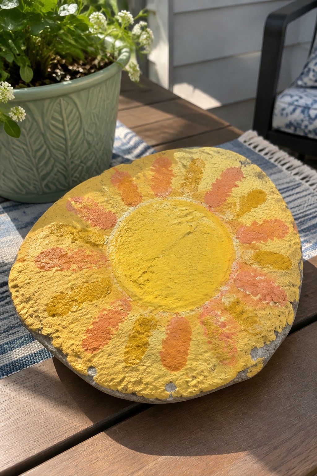 Painted stone sun with yellow-orange rays on wooden outdoor table