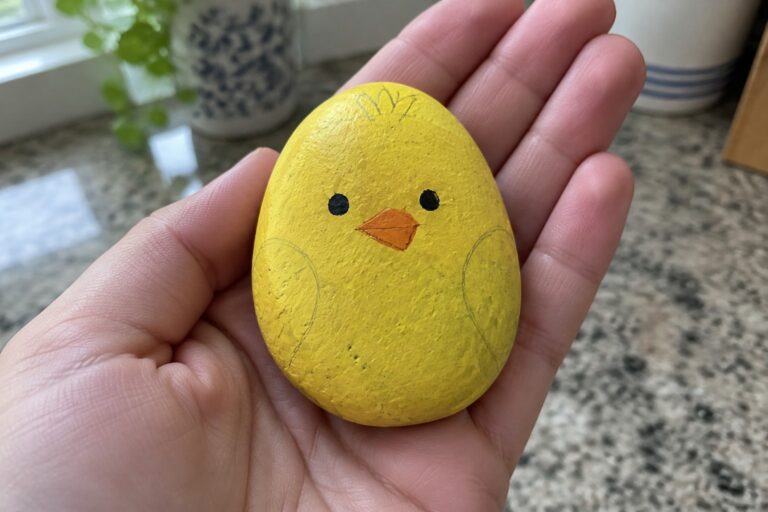 16 Rock Painting Ideas With Printable Templates for Easy Tracing Hand holding yellow painted rock chick with black eyes, orange beak and feet.