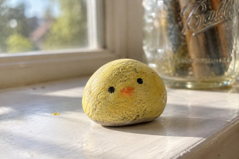 Yellow painted rock chick with orange beak on sunny white windowsill