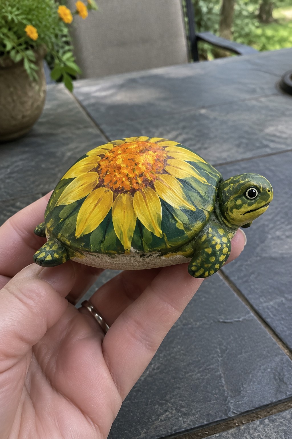 Hand holding a green turtle figurine with yellow sunflower on its shell.