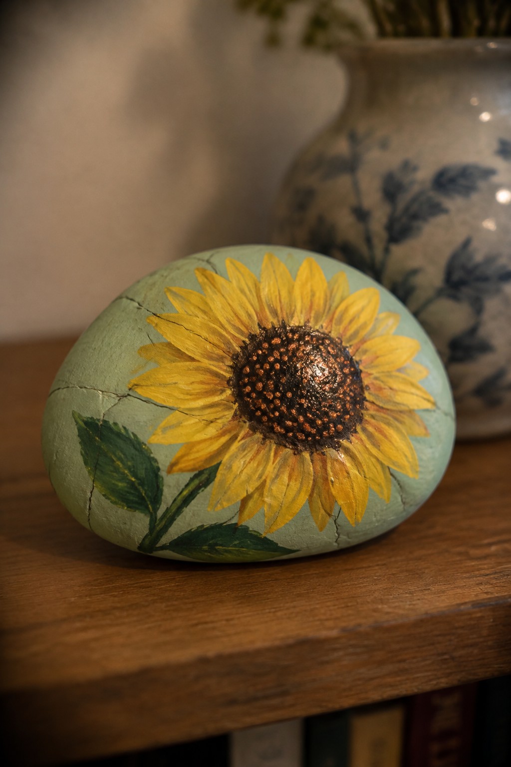 Painted cracked green rock with yellow sunflower on wooden surface beside vase