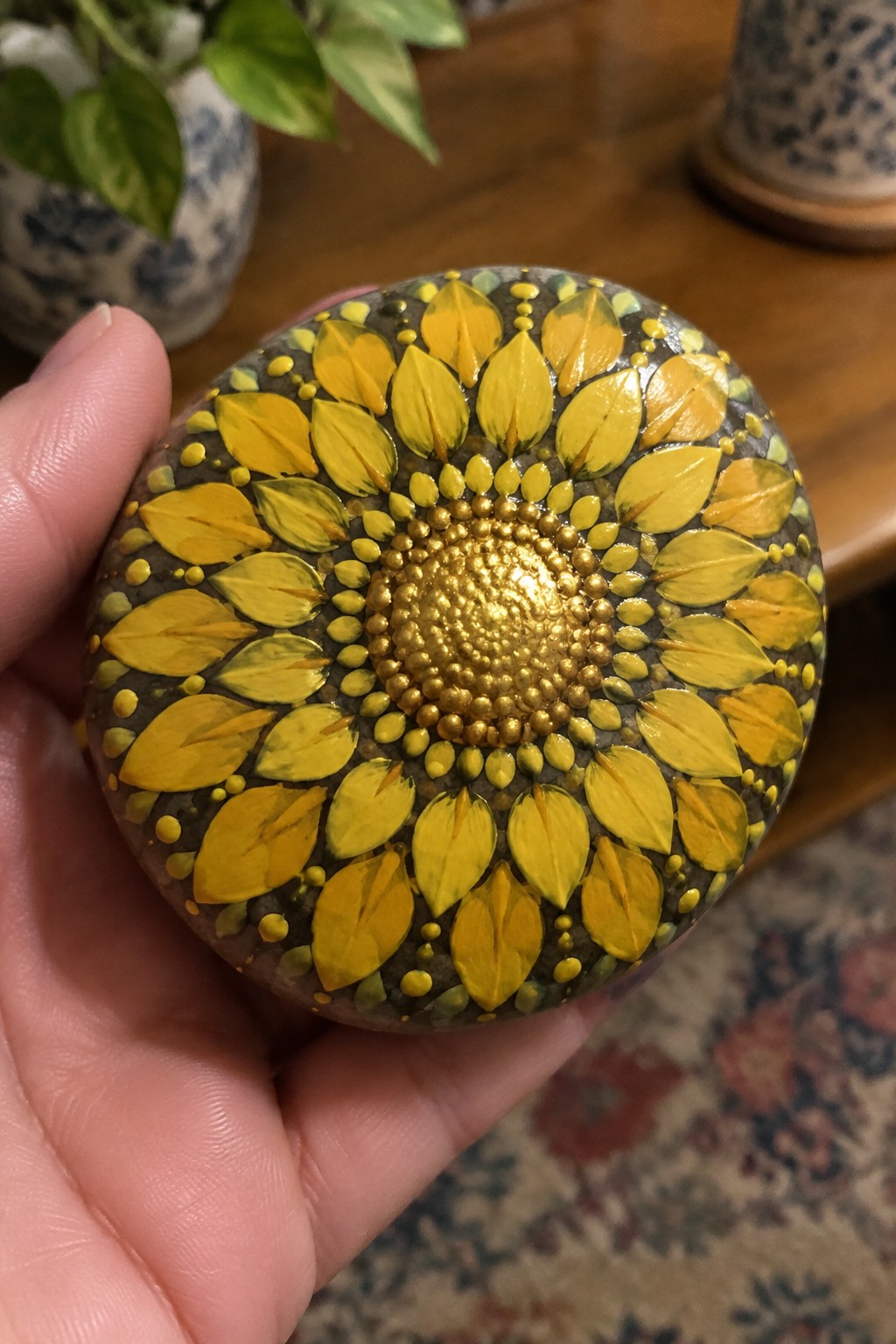 Hand holds round stone painted with yellow sunflower petals and gold dotted center.