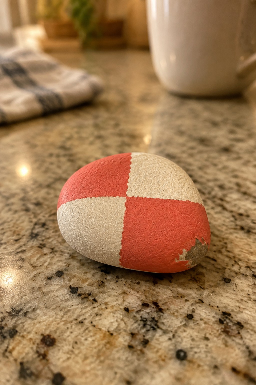 Red and white checkered painted rock on speckled granite countertop near white mug