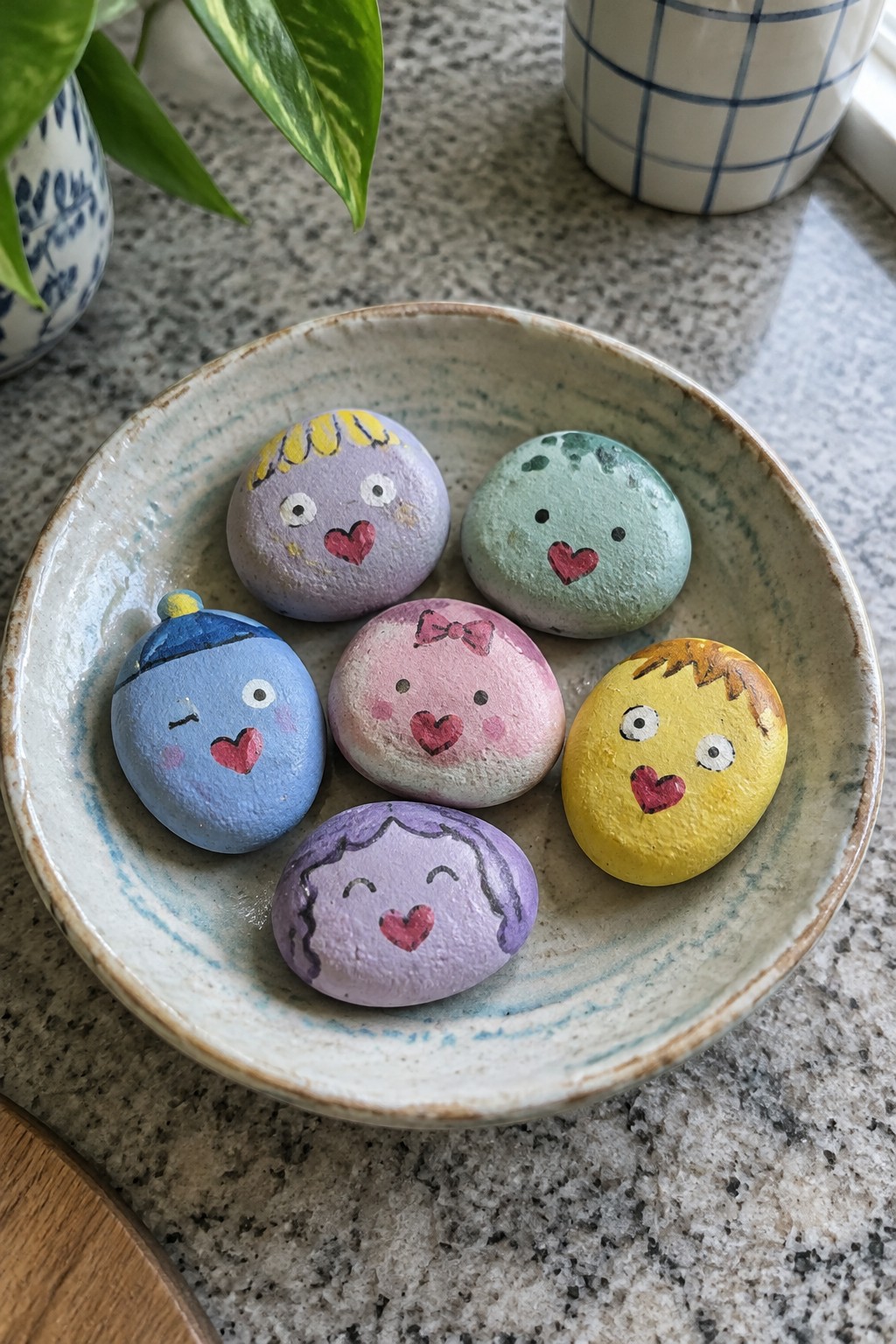Six colorful painted rocks with cartoon faces in a ceramic bowl.
