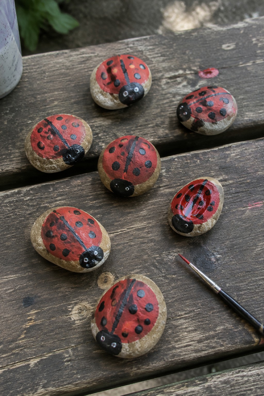 Painted ladybug rocks on wooden table beside red-tipped paintbrush