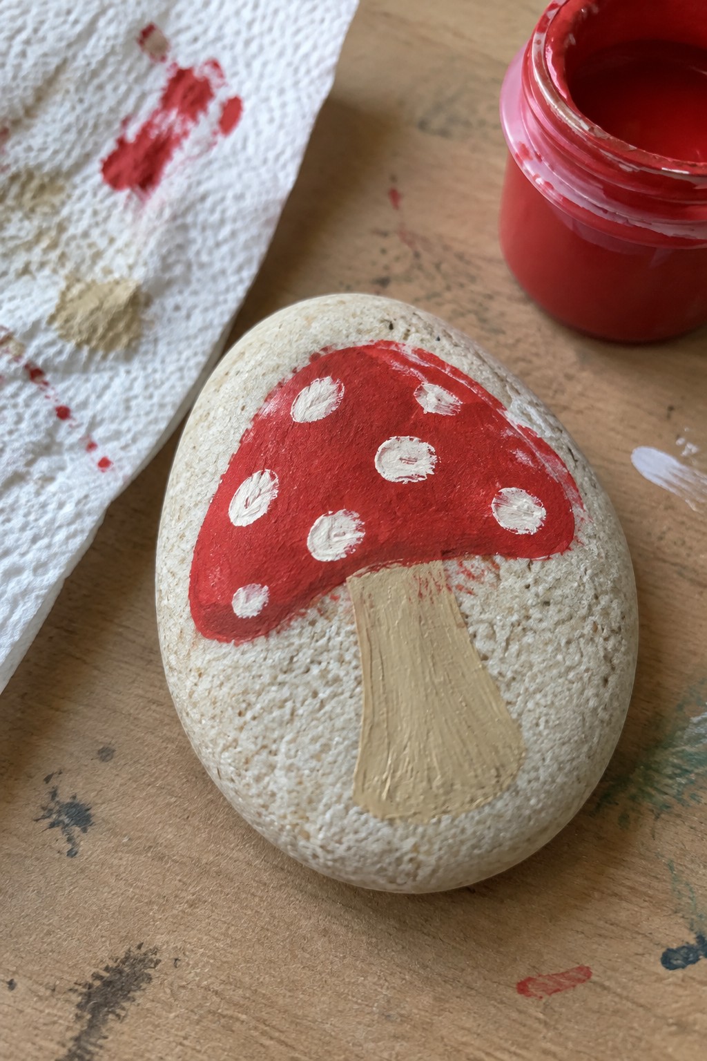 Painted rock as red mushroom with white dots and beige stem on wood