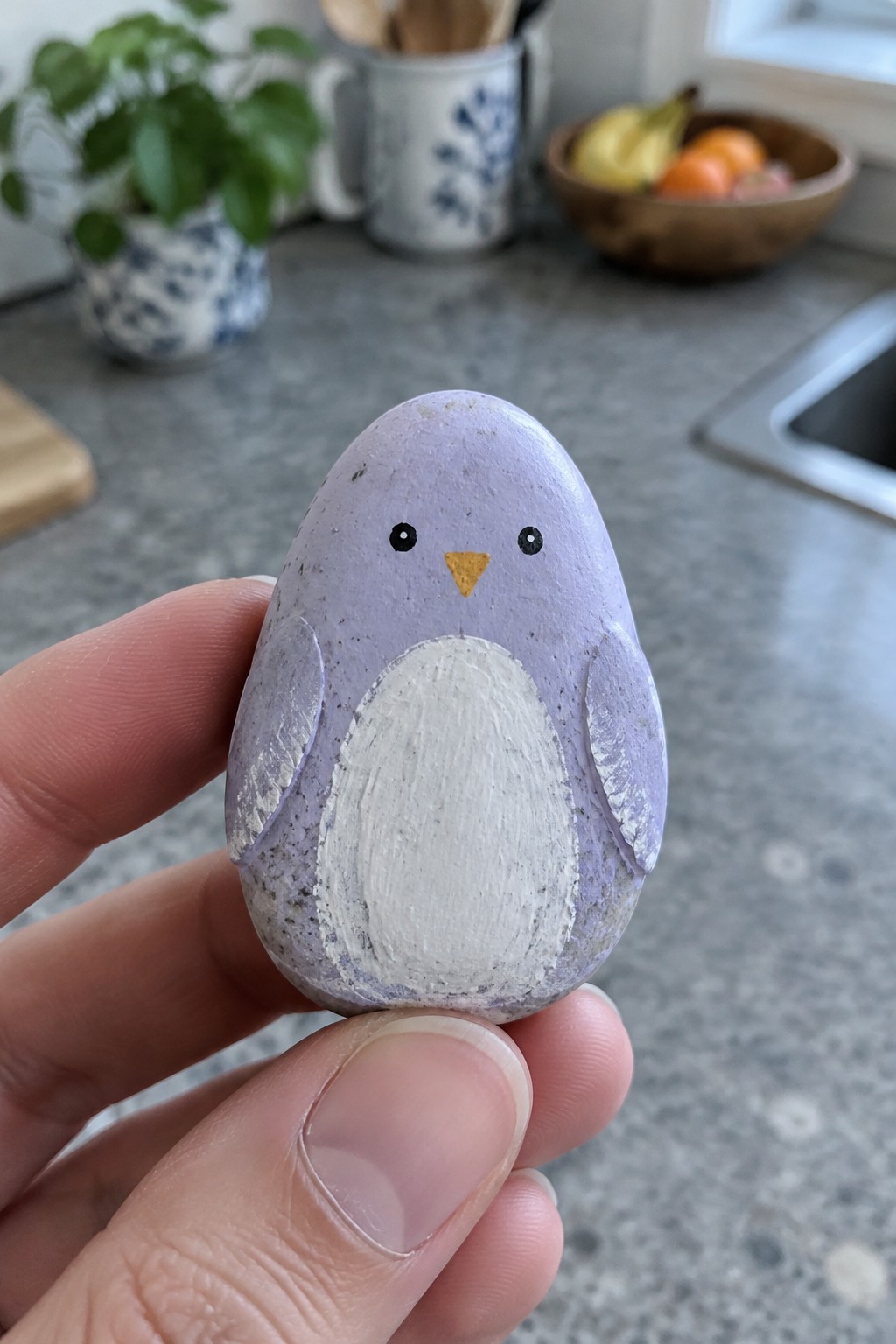 Hand holding small purple rock painted as penguin with white belly