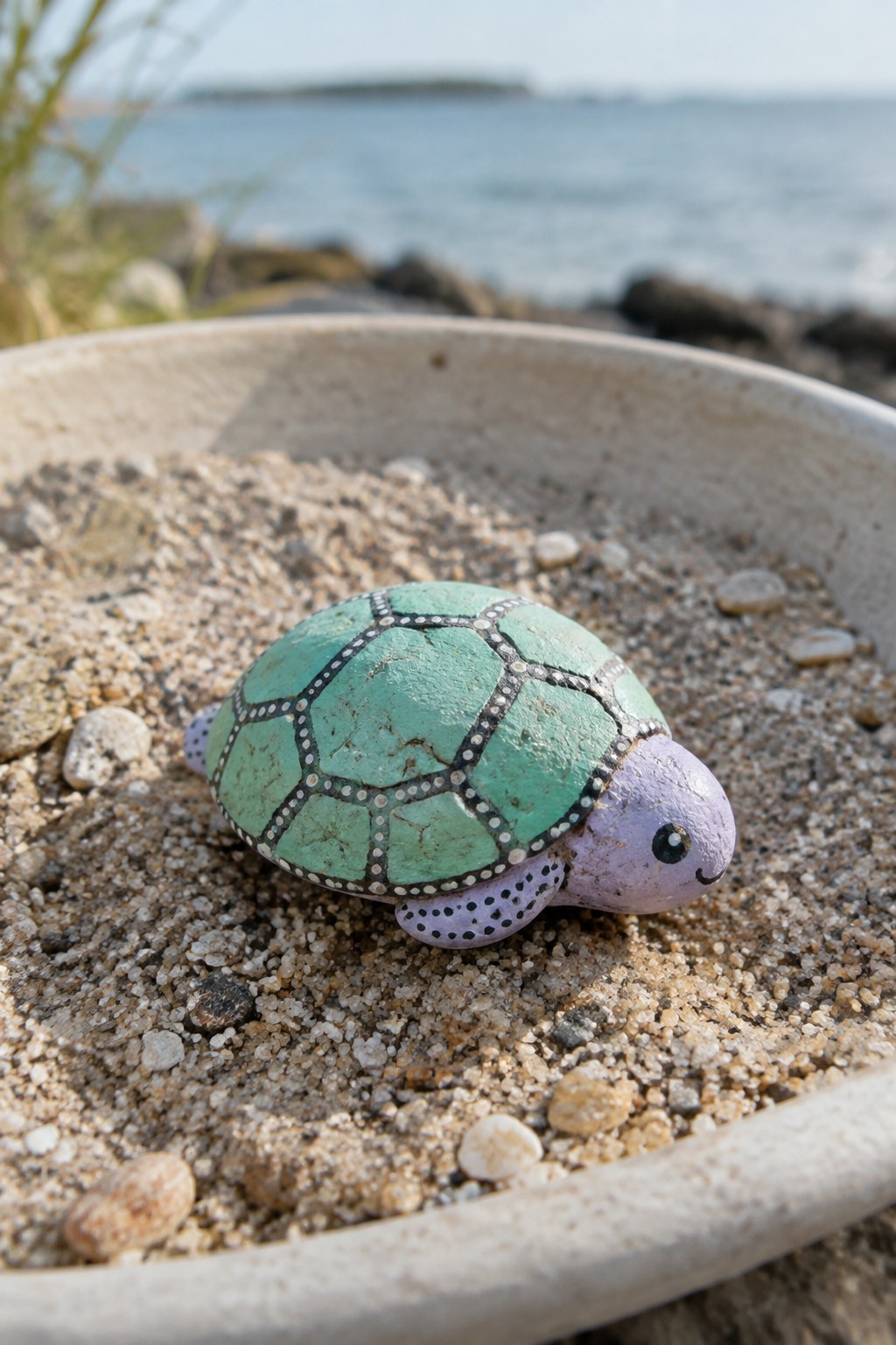 Painted rock turtle with green patterned shell and purple head on sand