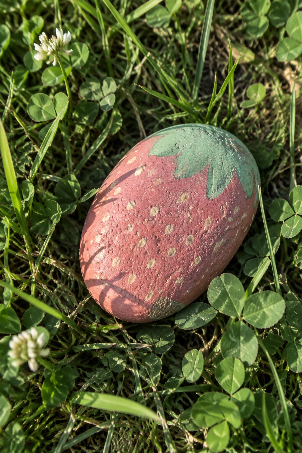 Painted red strawberry rock with green leaves amid clover in sunlit grass