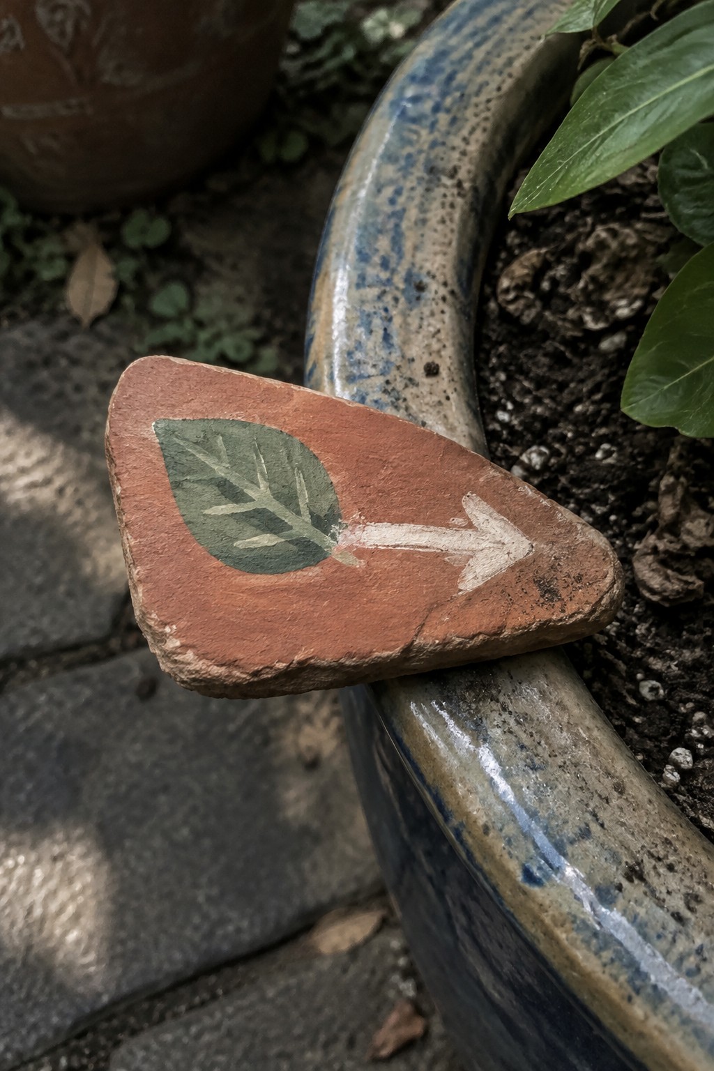 Terracotta shard with green leaf and white arrow resting on blue glazed pot rim
