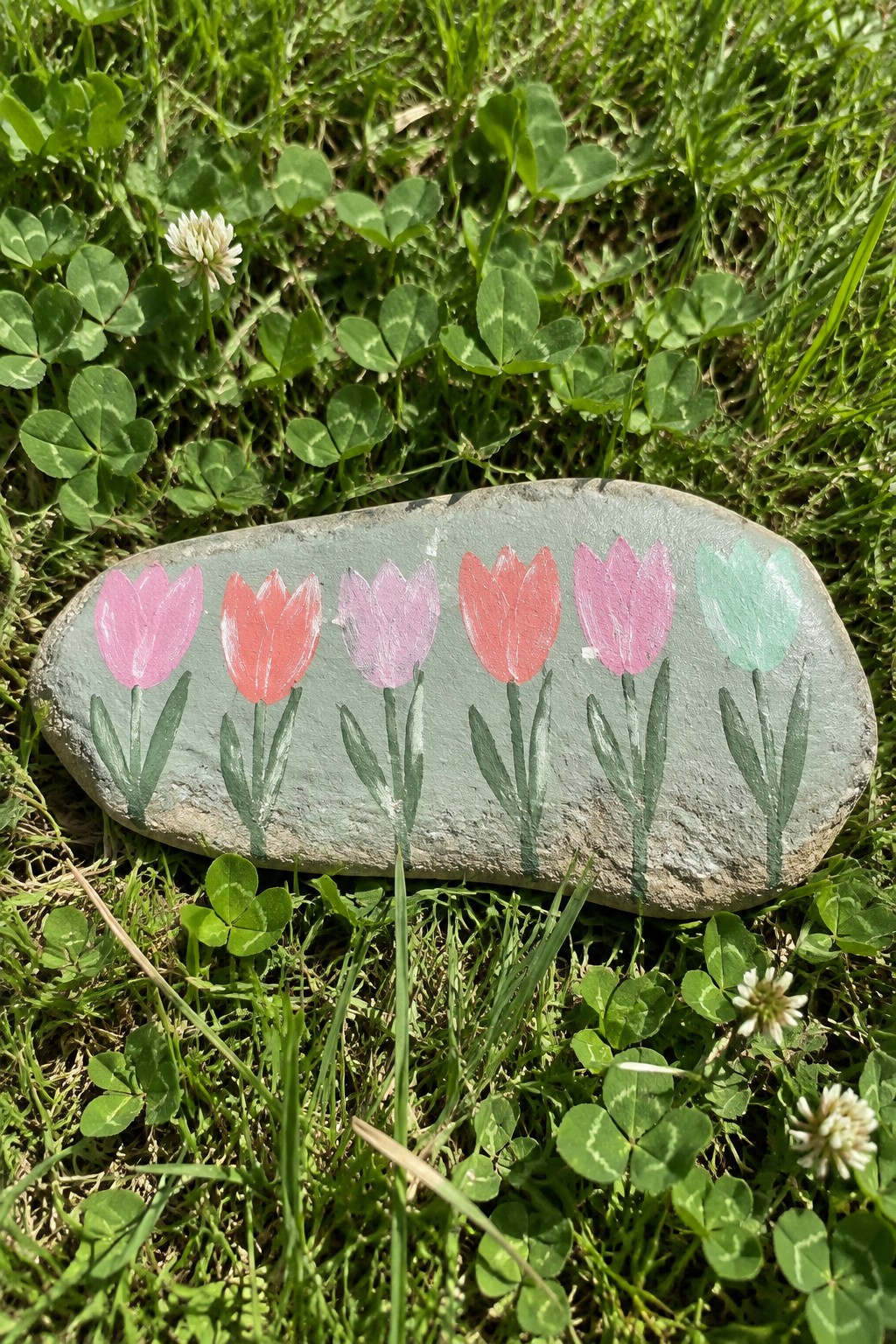 Gray rock painted with six colorful tulips on green clover grass.