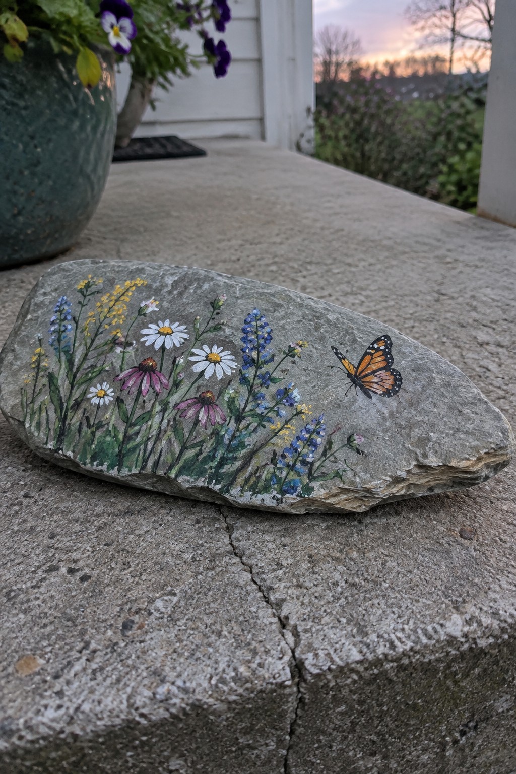 Painted rock with wildflowers and monarch butterfly on concrete porch step.