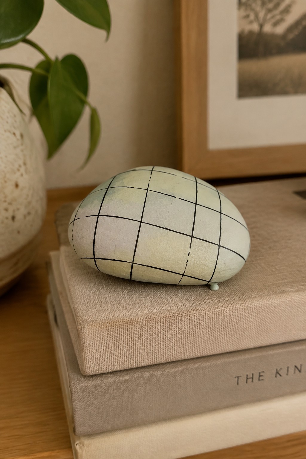 Oval stone painted light green with black grid lines on stacked books