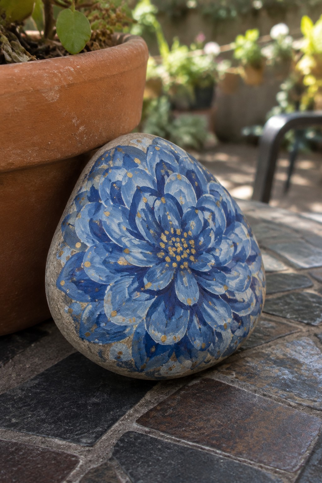 Blue painted flower with gold dots on stone beside terracotta pot on bricks