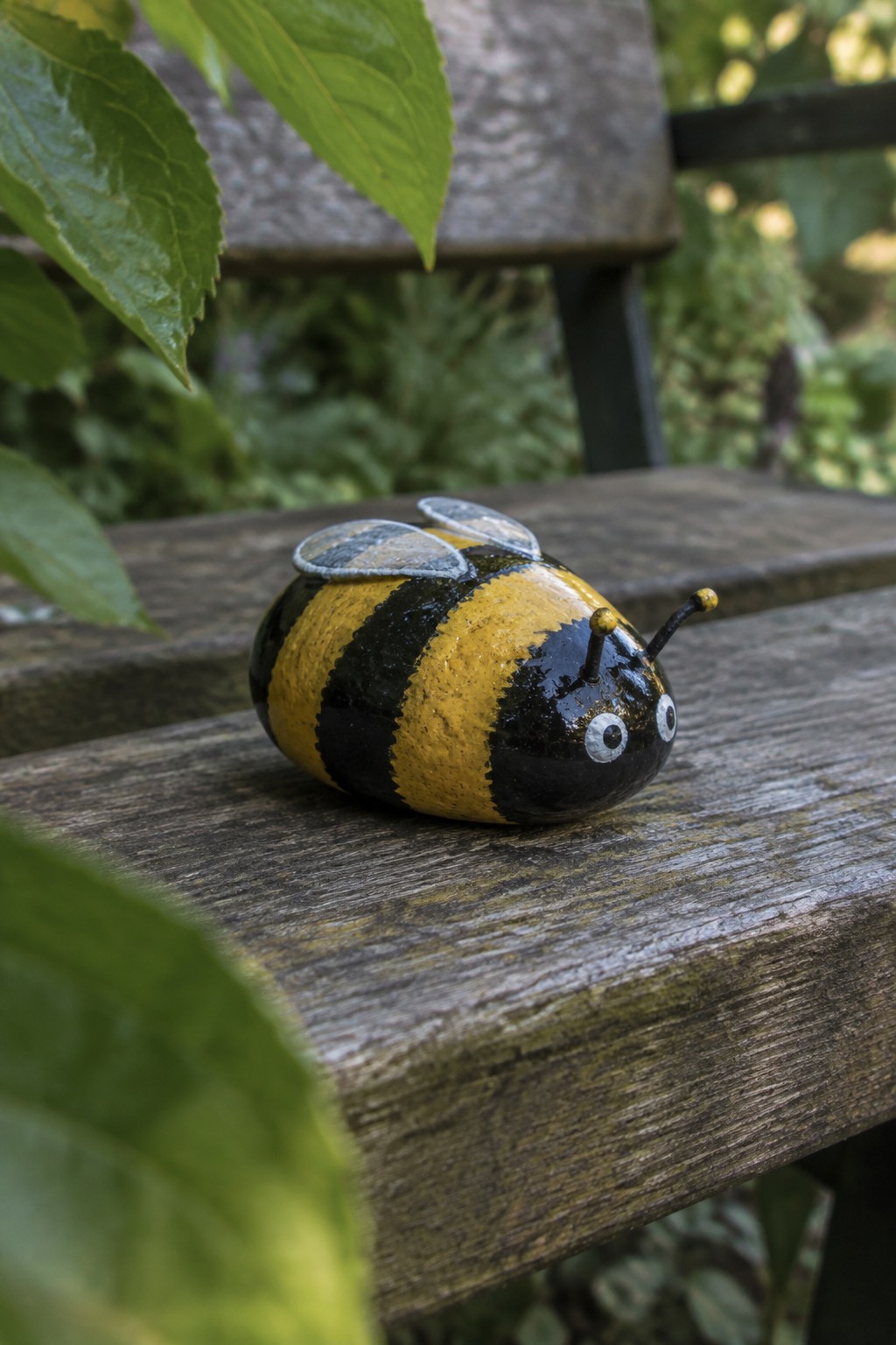 Bumblebee painted rock with black and yellow stripes on wooden bench
