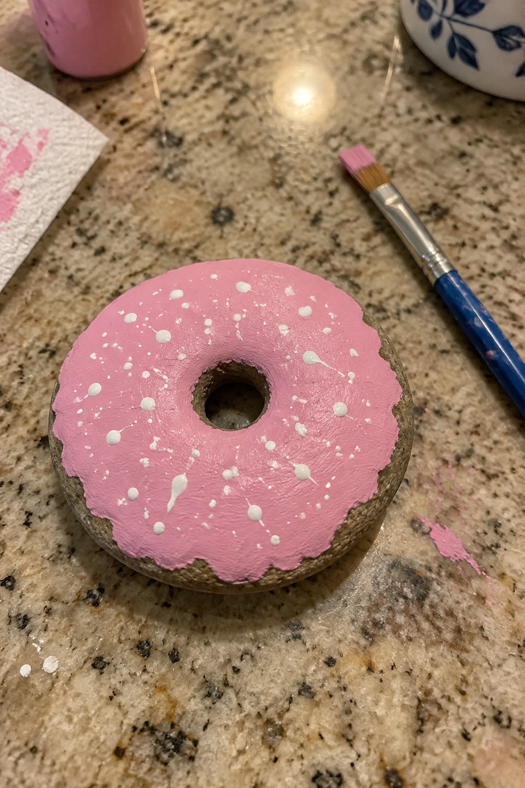 Pink-iced donut rock with white sprinkles beside paintbrush on granite counter