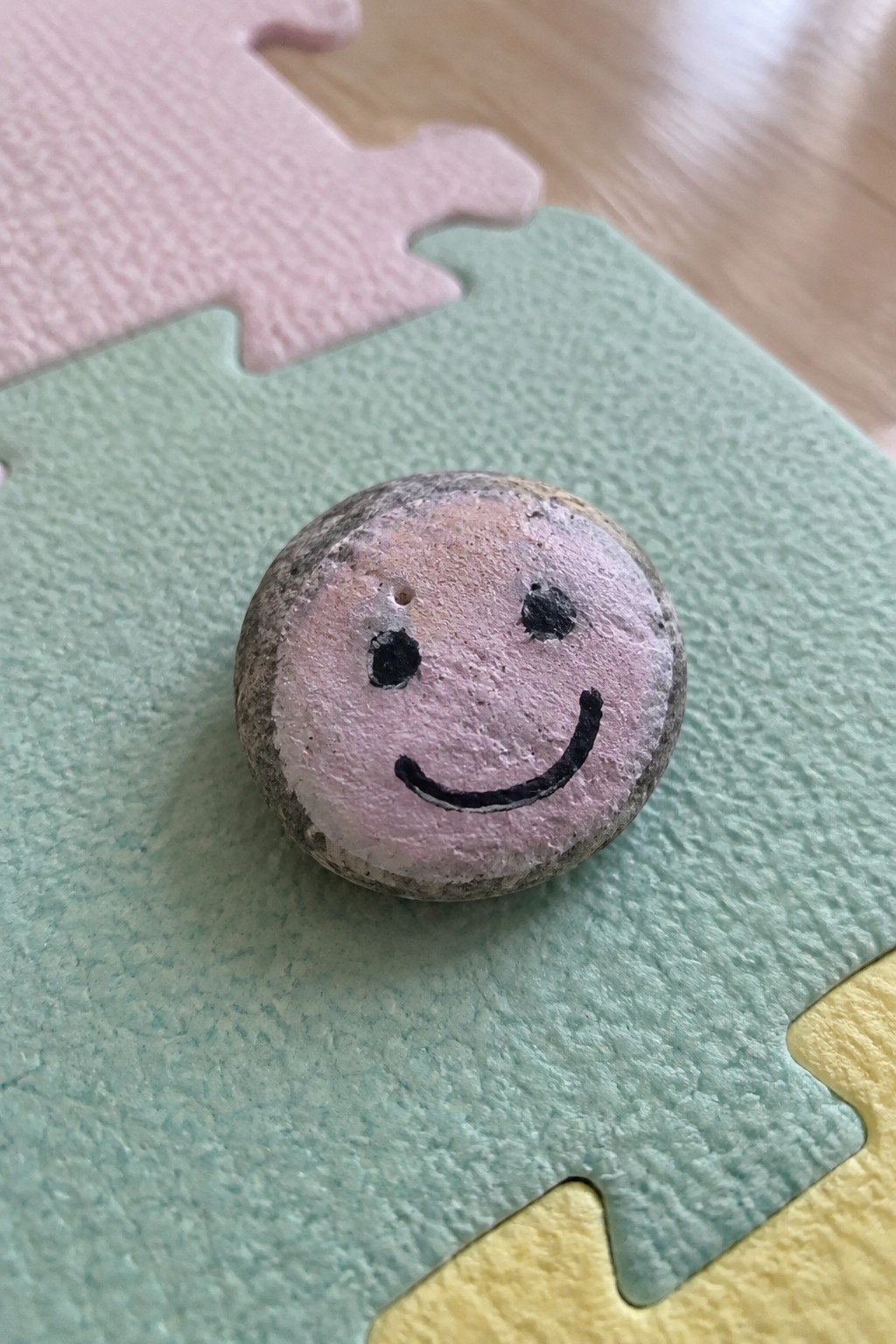 Smiling face painted on round stone atop green foam puzzle mat