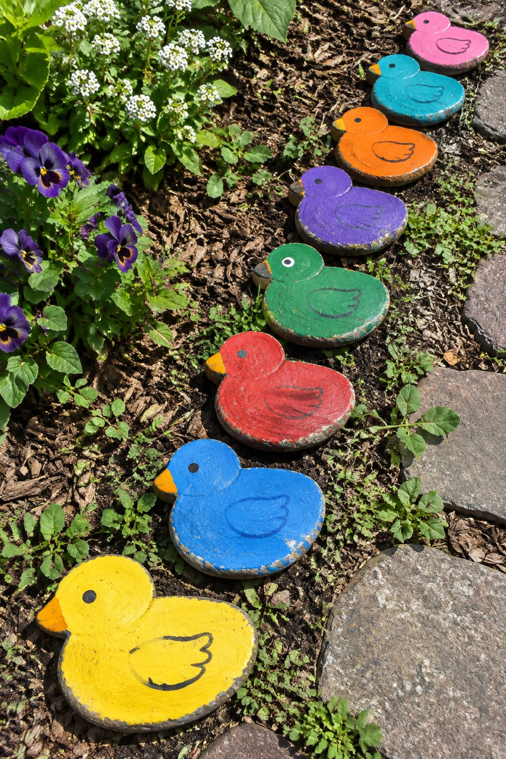 Colorful painted duck stepping stones in a row along a garden path