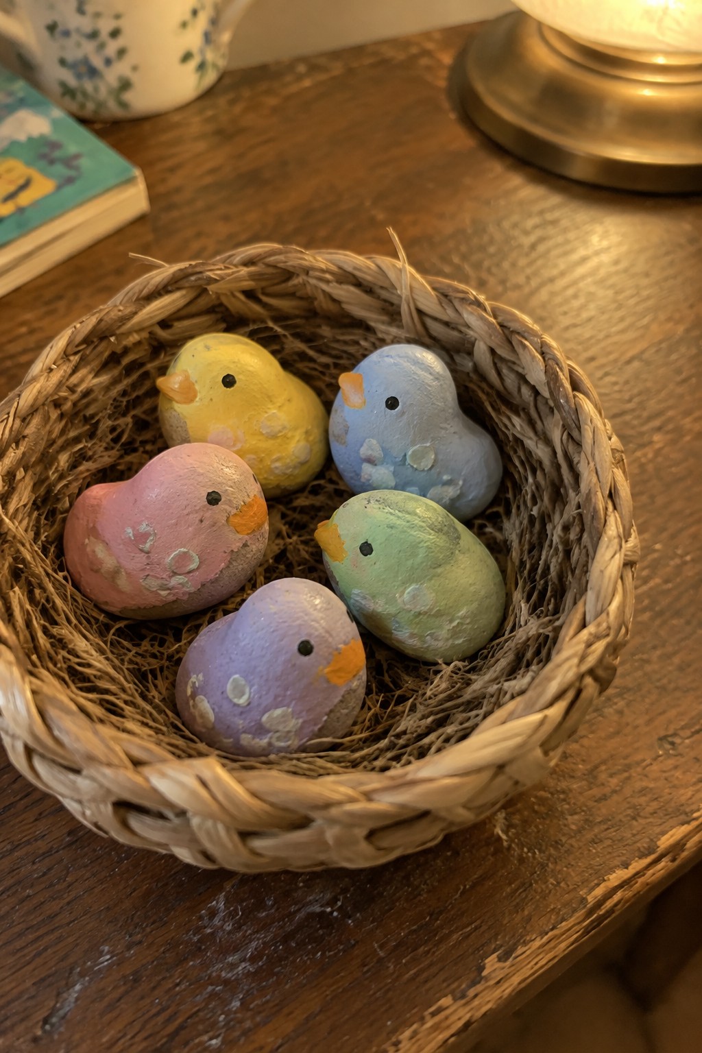Five colorful painted stone birds nestled in a woven basket on wood