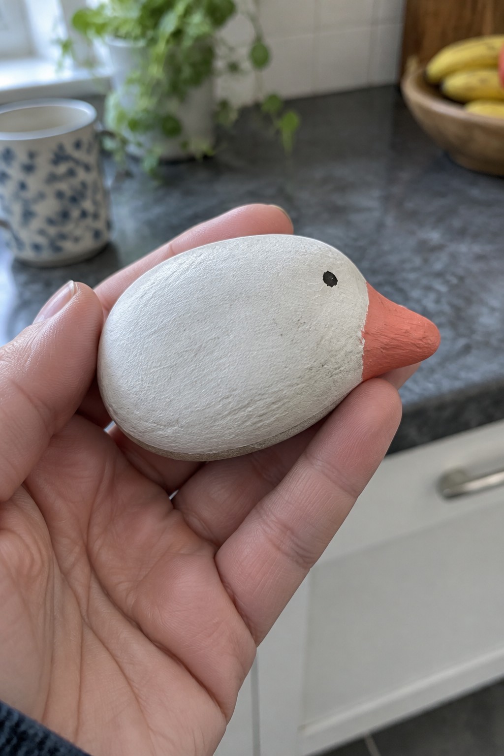 Hand holding small white painted bird figurine with orange beak and black eye