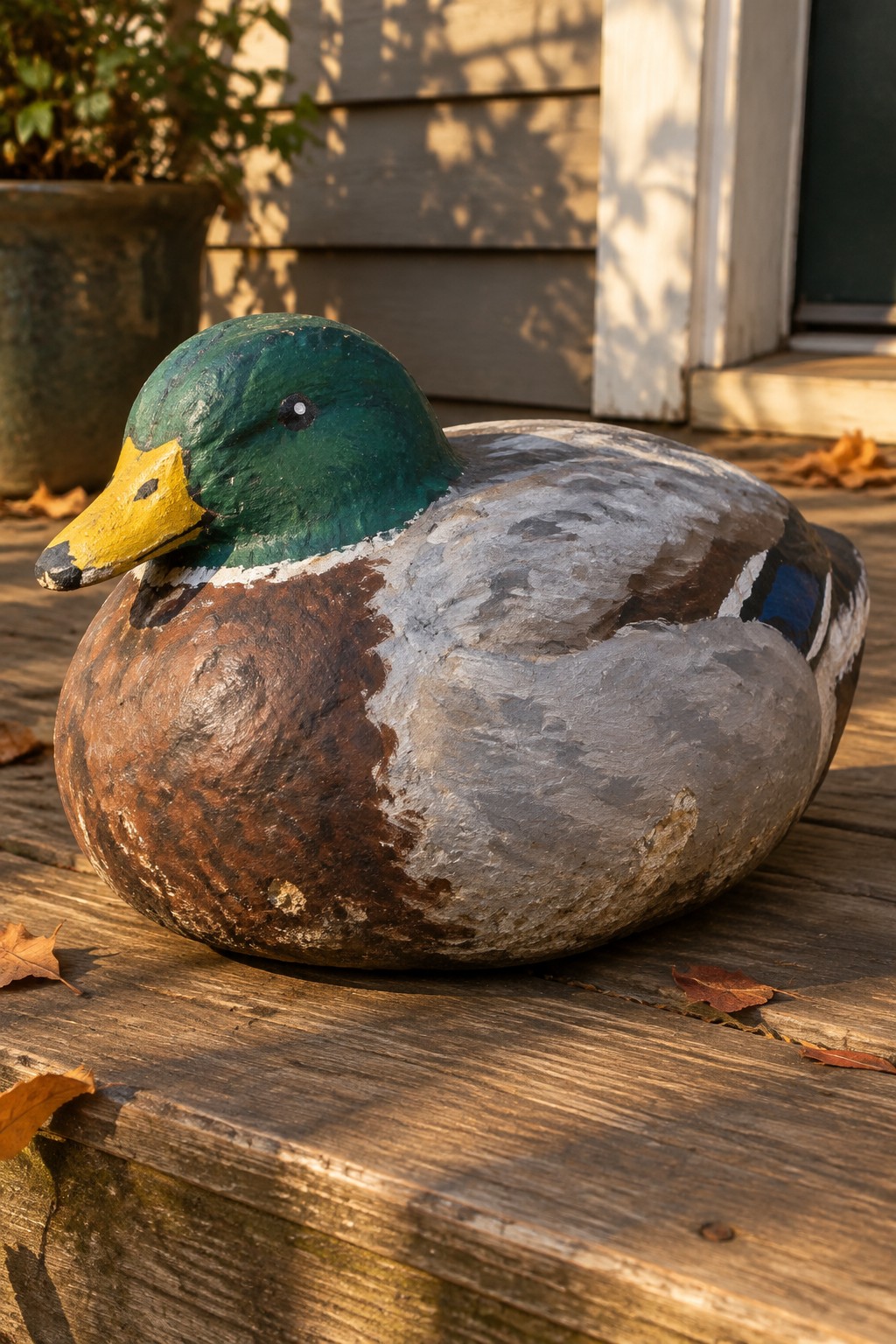 Weathered wooden mallard duck decoy on deck with autumn leaves