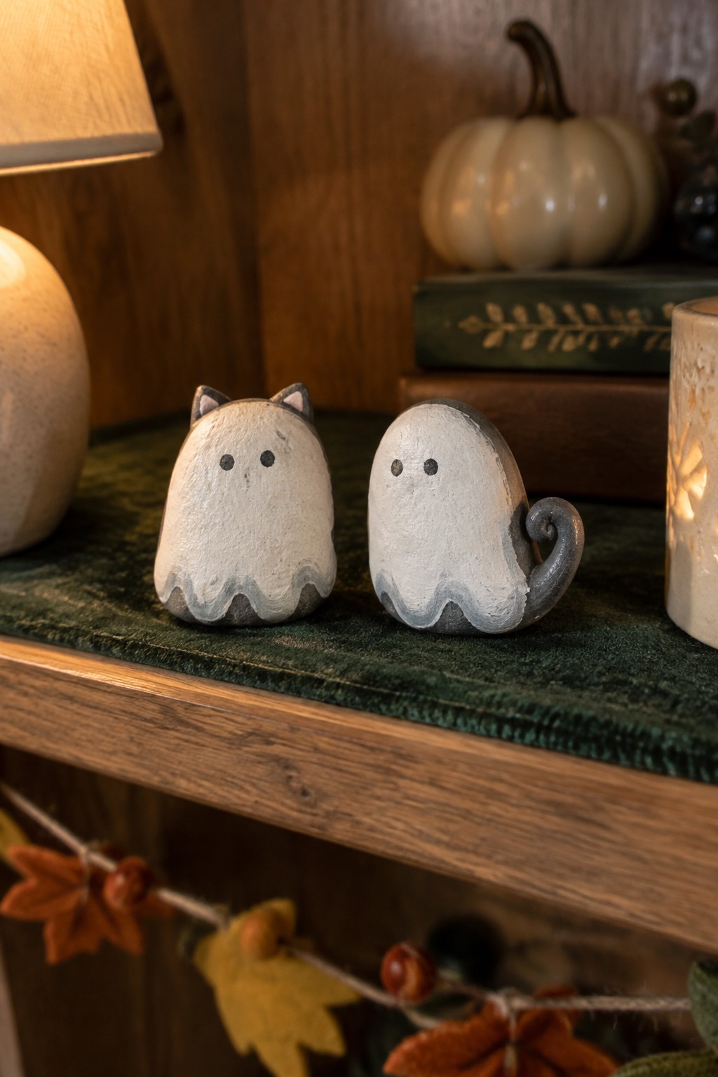 Two cat ghost figurines on green velvet shelf with autumn decor