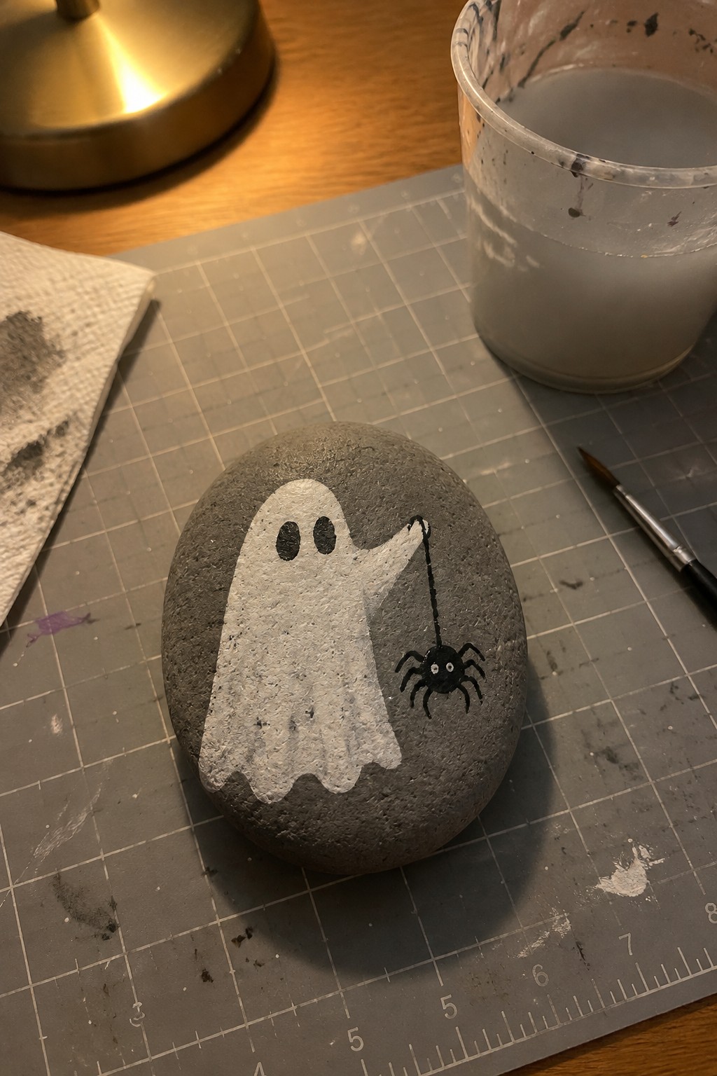 Gray rock painted with white ghost holding string to black spider on mat