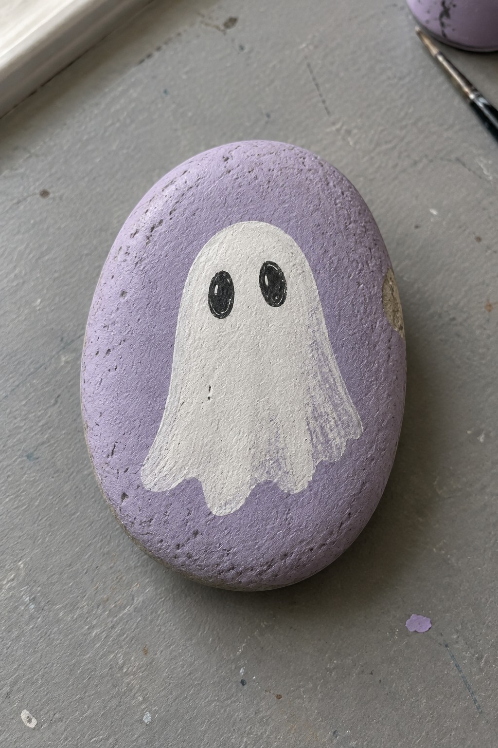 Purple rock painted with white ghost and black oval eyes