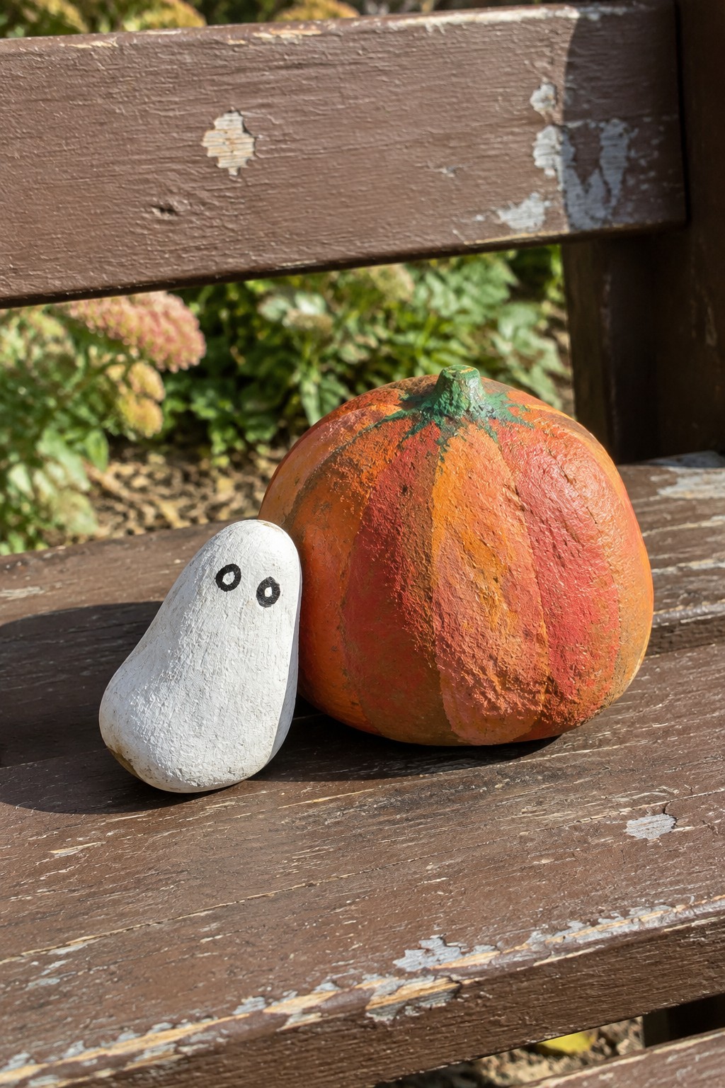 Painted white ghost rock beside orange-red pumpkin on weathered wooden bench