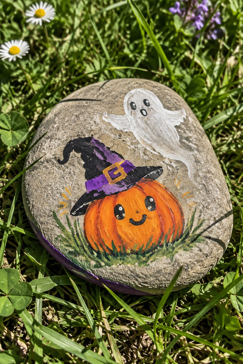 Painted rock with orange pumpkin in purple witch hat and white ghost on grass