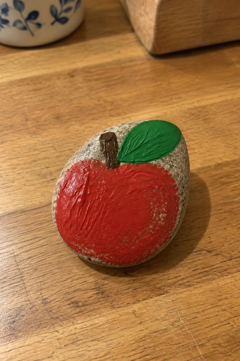 Painted rock resembling red apple with green leaf and brown stem on wood