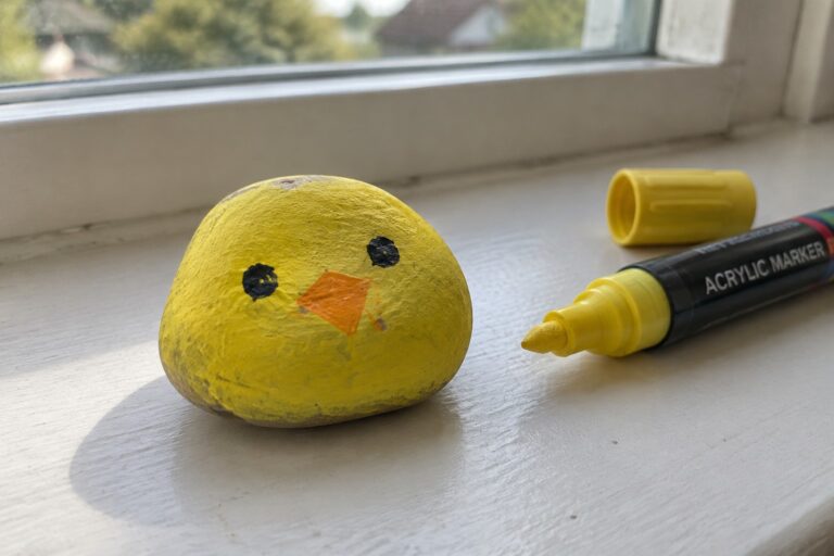 Yellow chick rock with black eyes and orange beak beside yellow marker on windowsill
