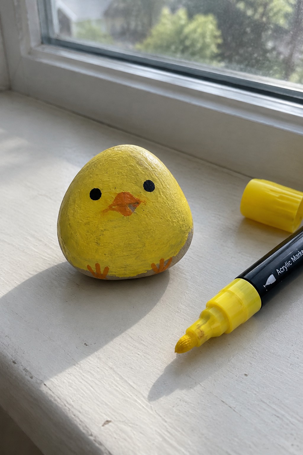 Yellow chick rock with black eyes and orange beak beside yellow marker on windowsill