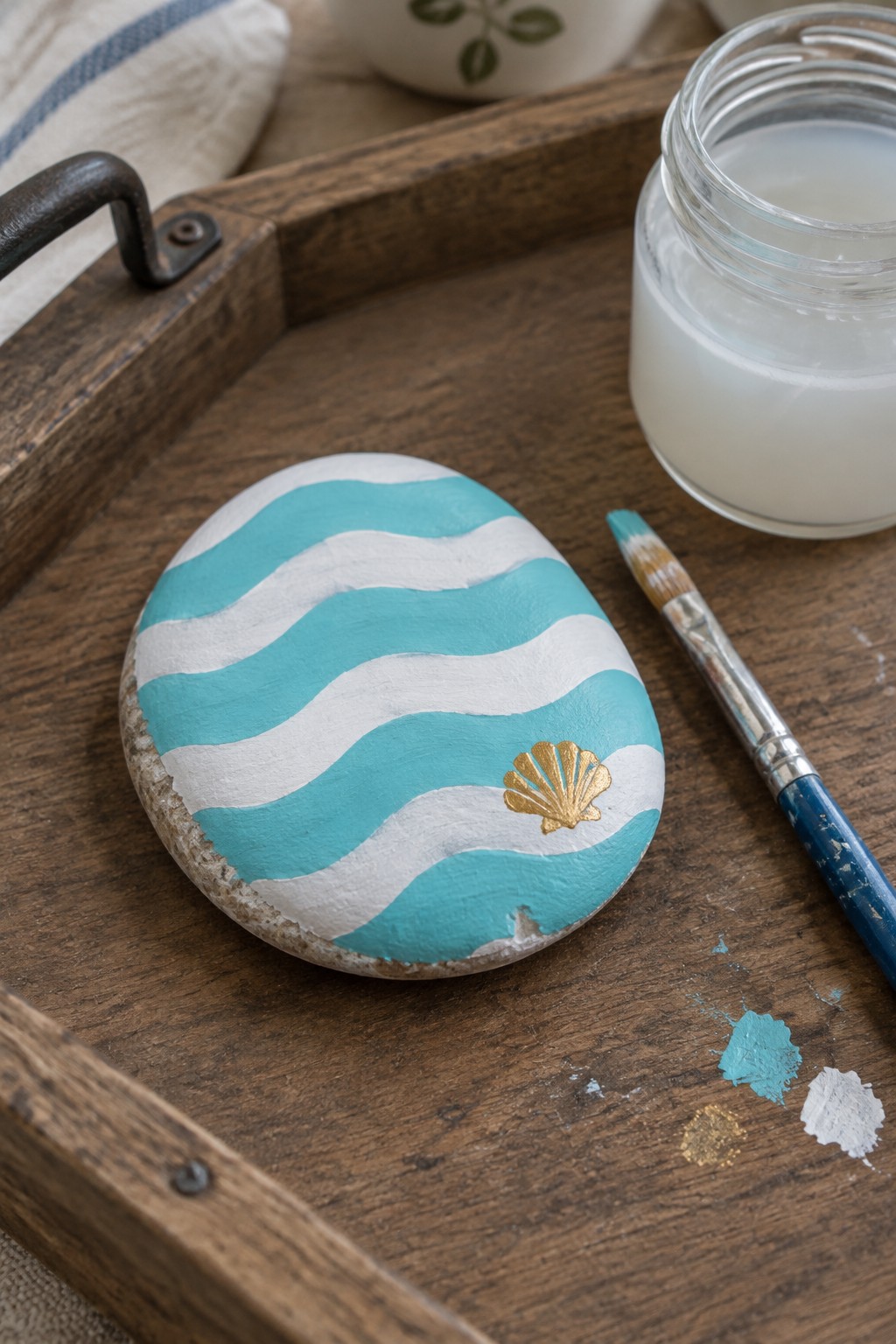 Wavy turquoise and white painted stone with gold seashell on wooden tray