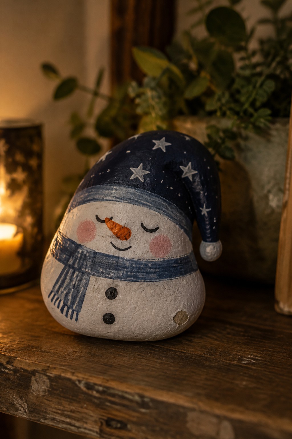 Painted rock snowman wearing blue starry nightcap and striped scarf on wood