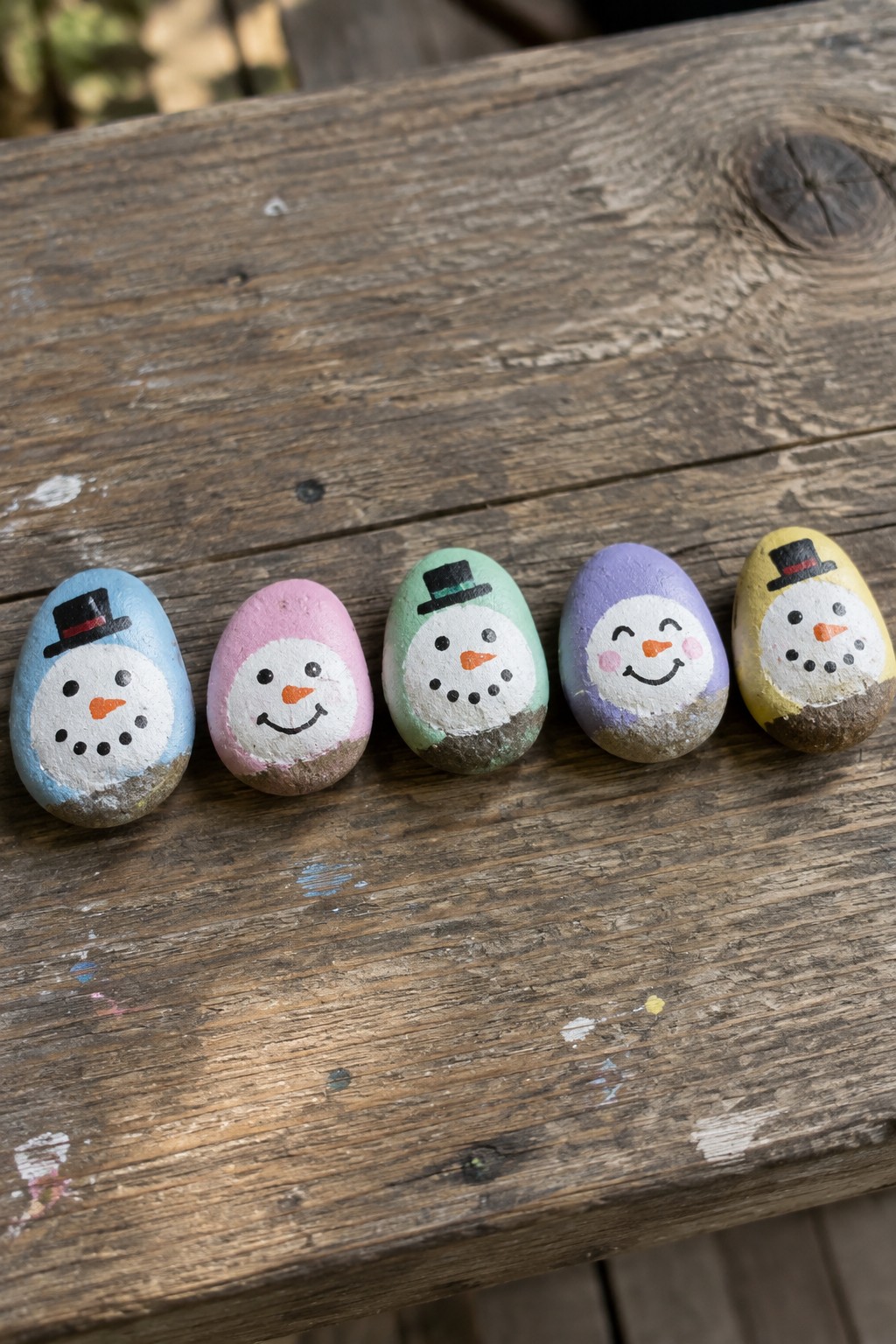 Five colorful painted rocks as snowmen with hats on wooden table.