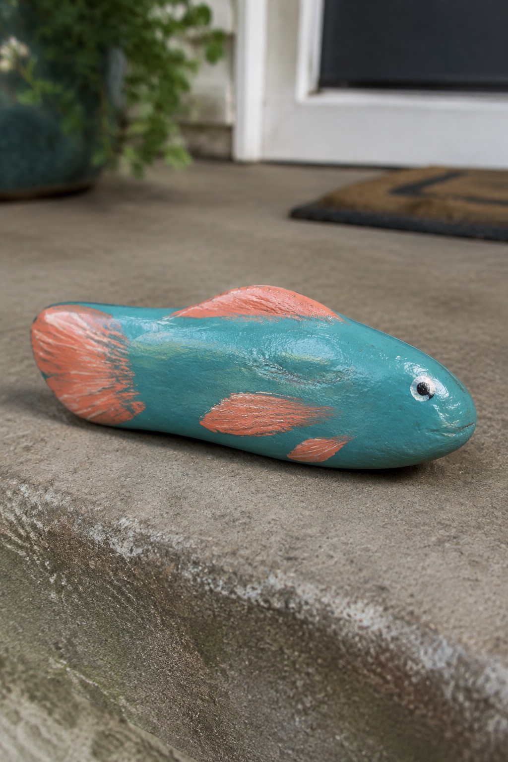 Turquoise painted rock fish with orange fins on concrete step.
