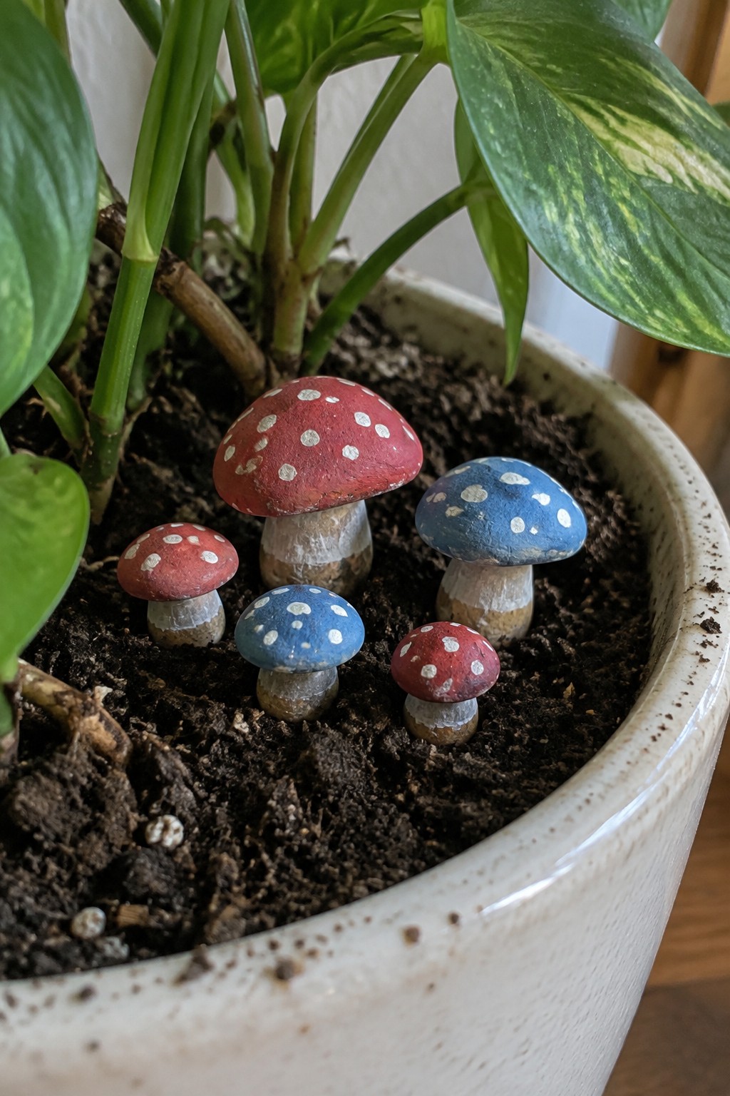 Painted red and blue spotted mushrooms nestled in potted plant soil