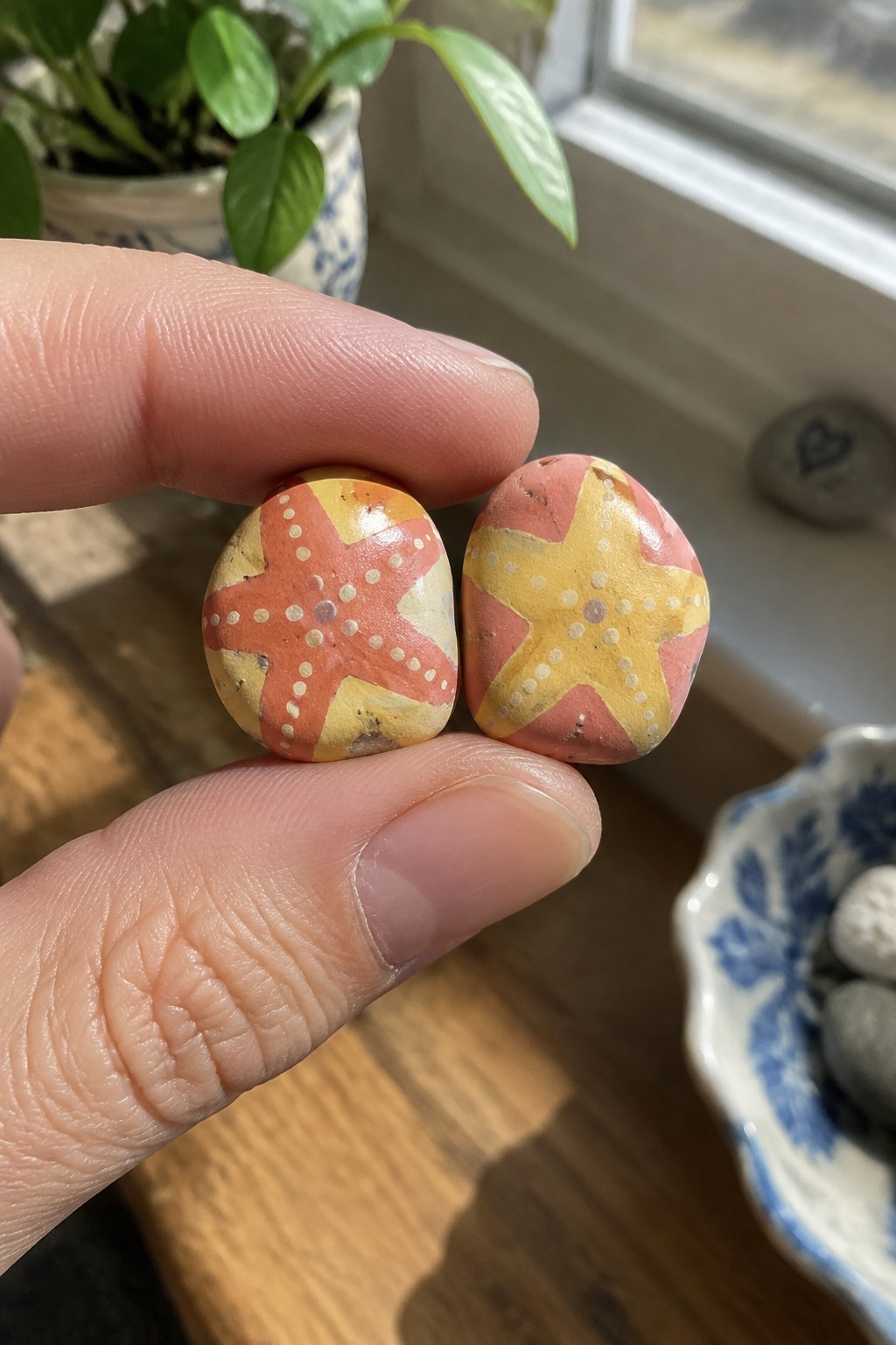 Fingers holding two small rocks painted with yellow and pink starfish