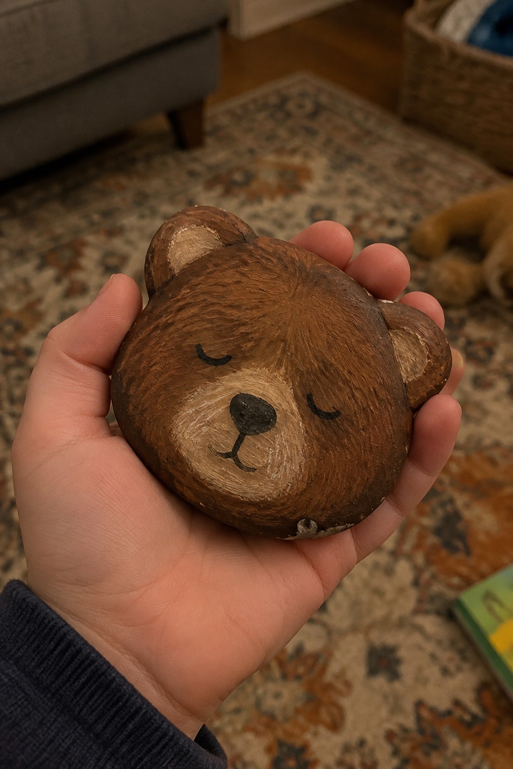 Hand in navy sleeve holding brown wooden bear figurine with closed eyes.