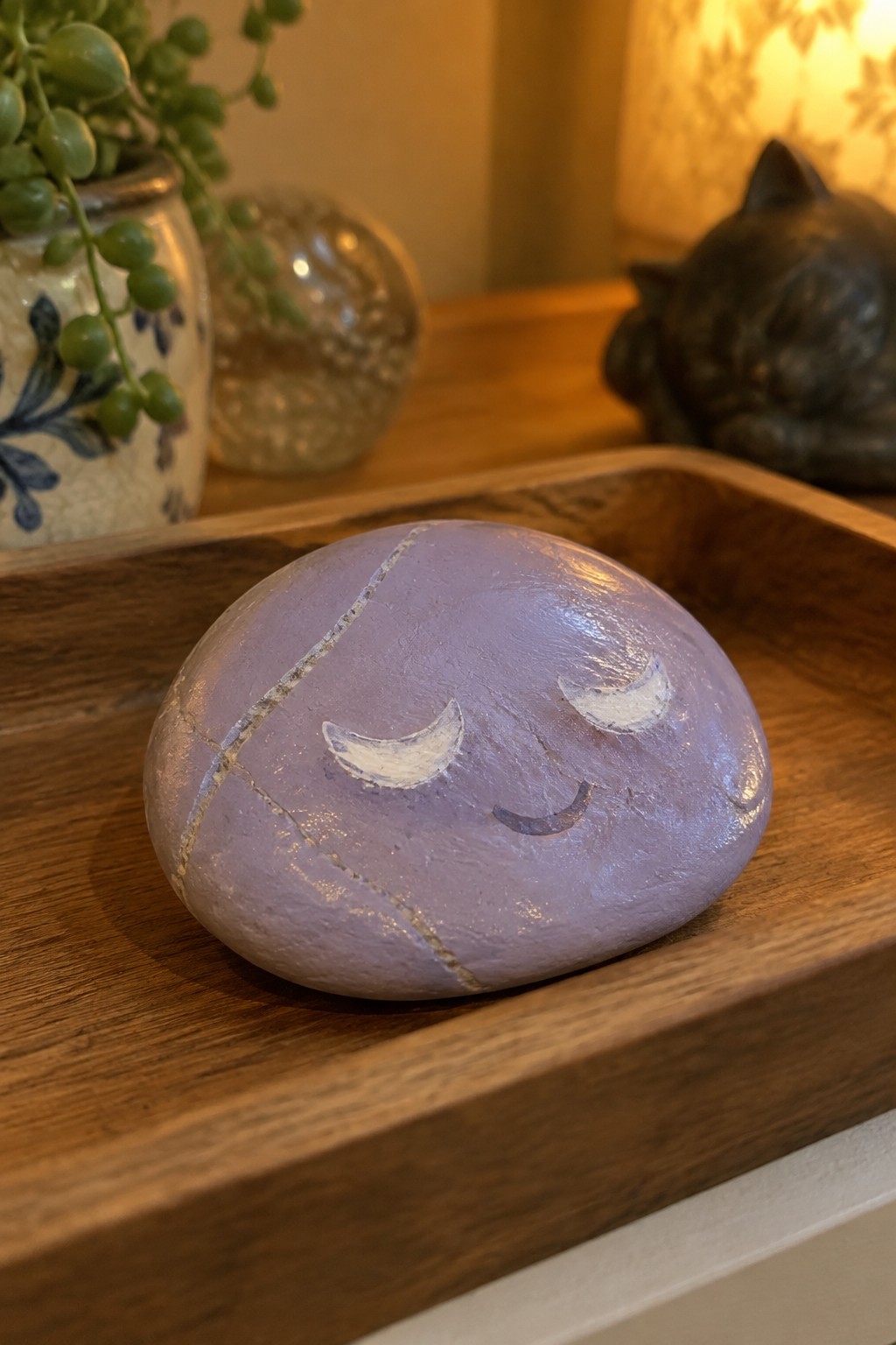 Painted purple rock with crescent eyes and smile on wooden tray