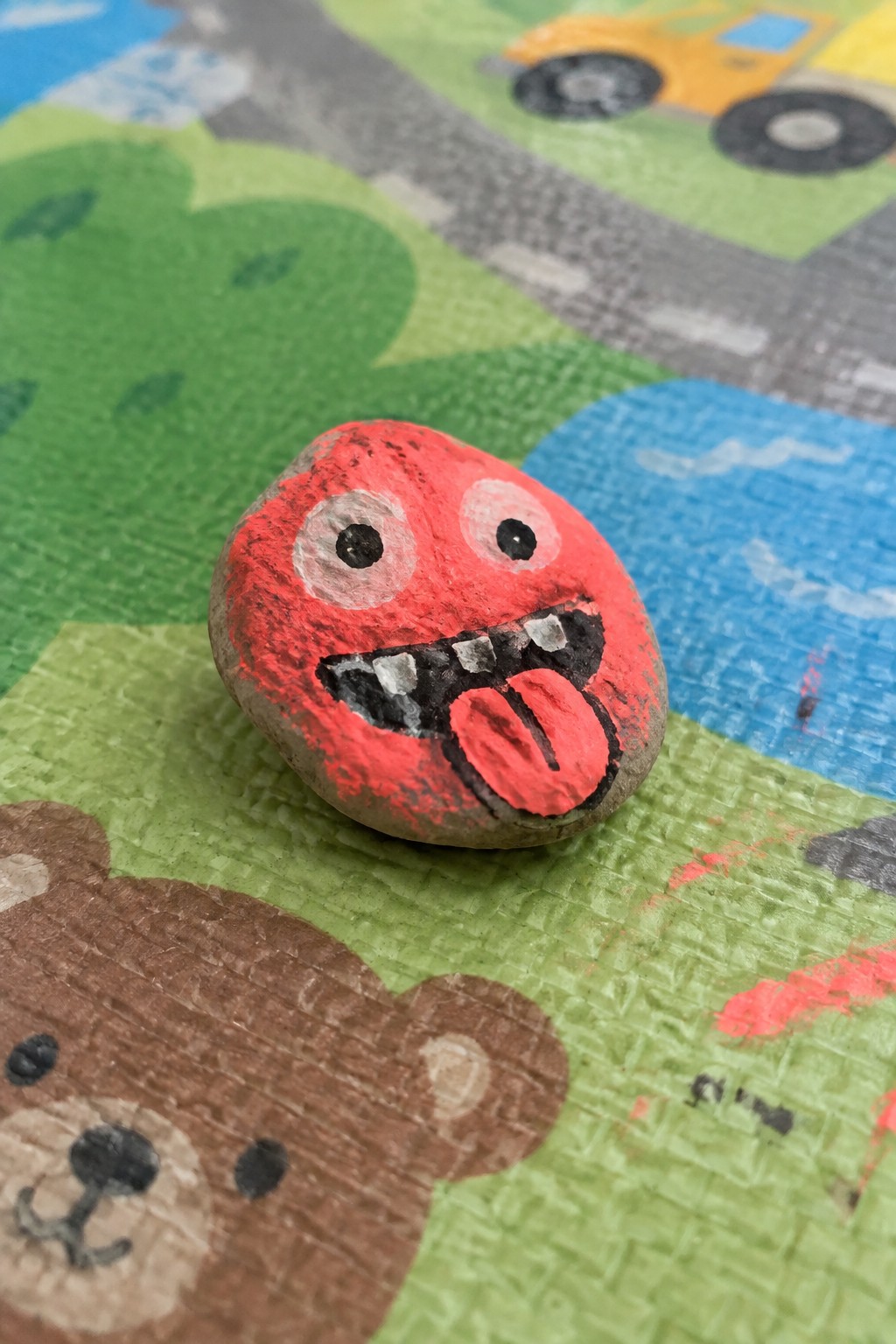 Red painted rock with cartoon monster face and tongue on play mat