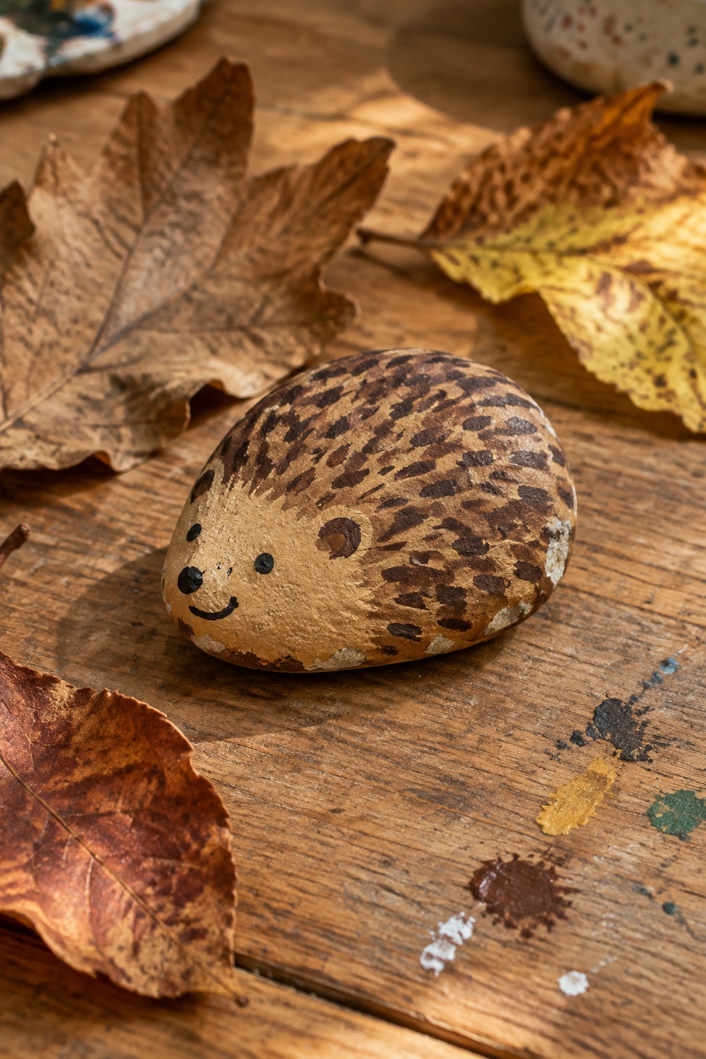 Painted hedgehog rock with smiling face amid autumn leaves on wooden table