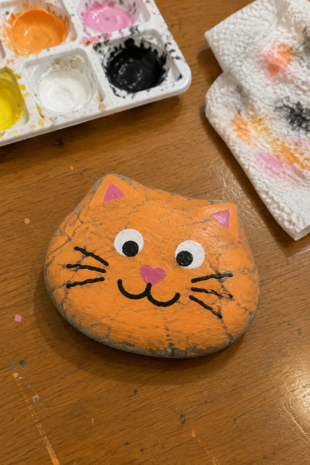 Orange painted cat rock beside paint palette and stained paper towel on wood