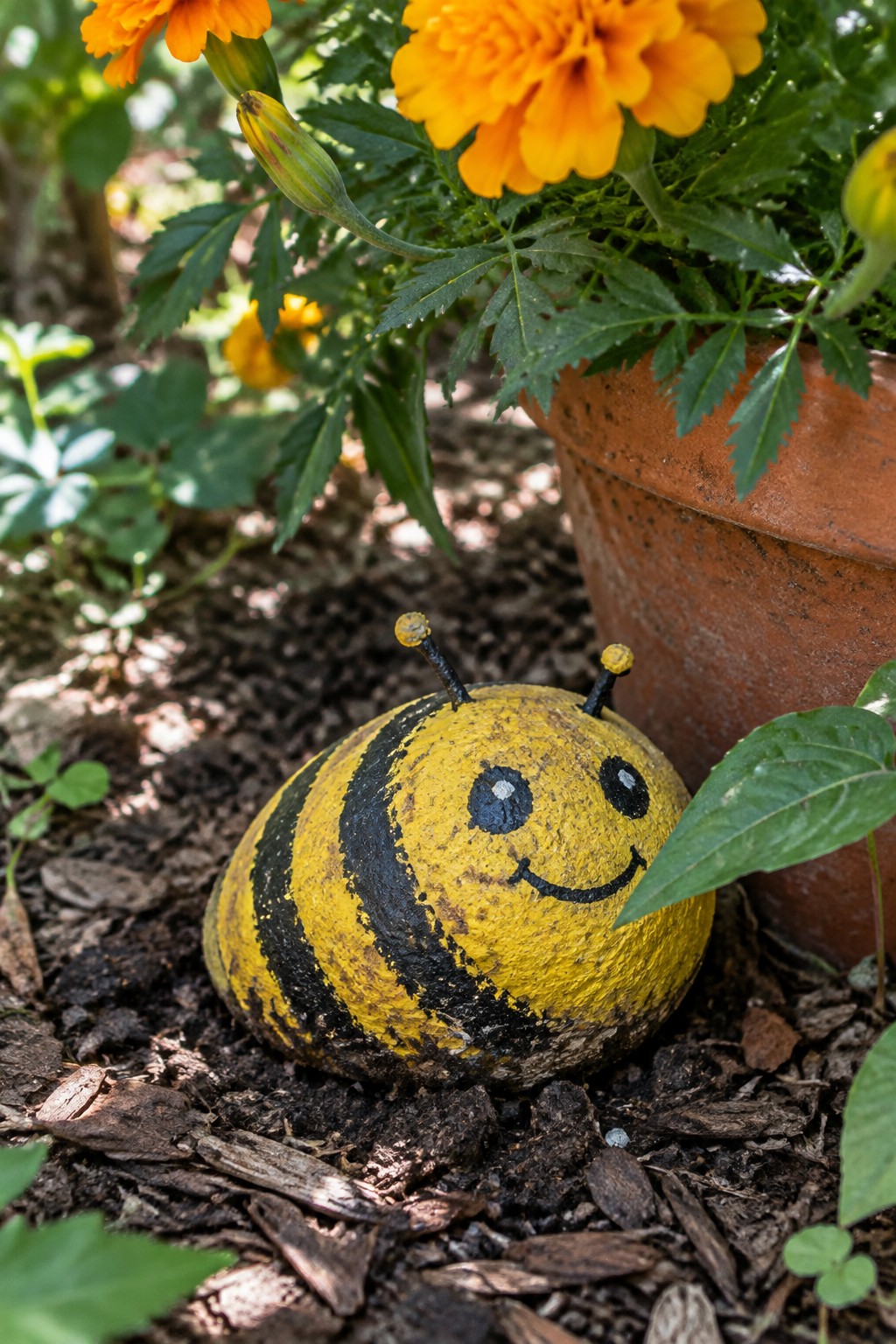 Smiling yellow-and-black striped bee rock beside orange marigolds in terracotta pot