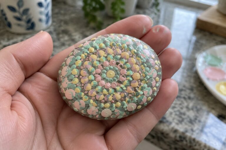 20 Rock Dot Painting Ideas Using Repeating Mandala Patterns Hand holding oval stone painted with pastel green, yellow, and pink dots